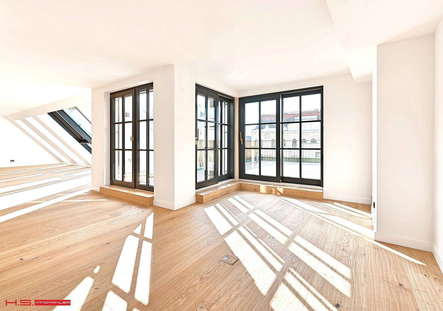 Geräumiger Wohnbereich mit Holzboden und mehreren Fenstertüren, die den Raum hell und offen wirken lassen.