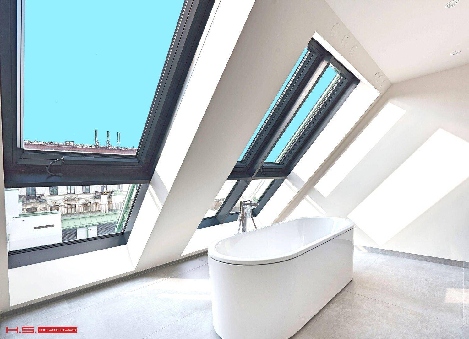 Modernes Badezimmer mit freistehender Badewanne, grauen Fliesen und großen Dachfenstern für viel Licht.