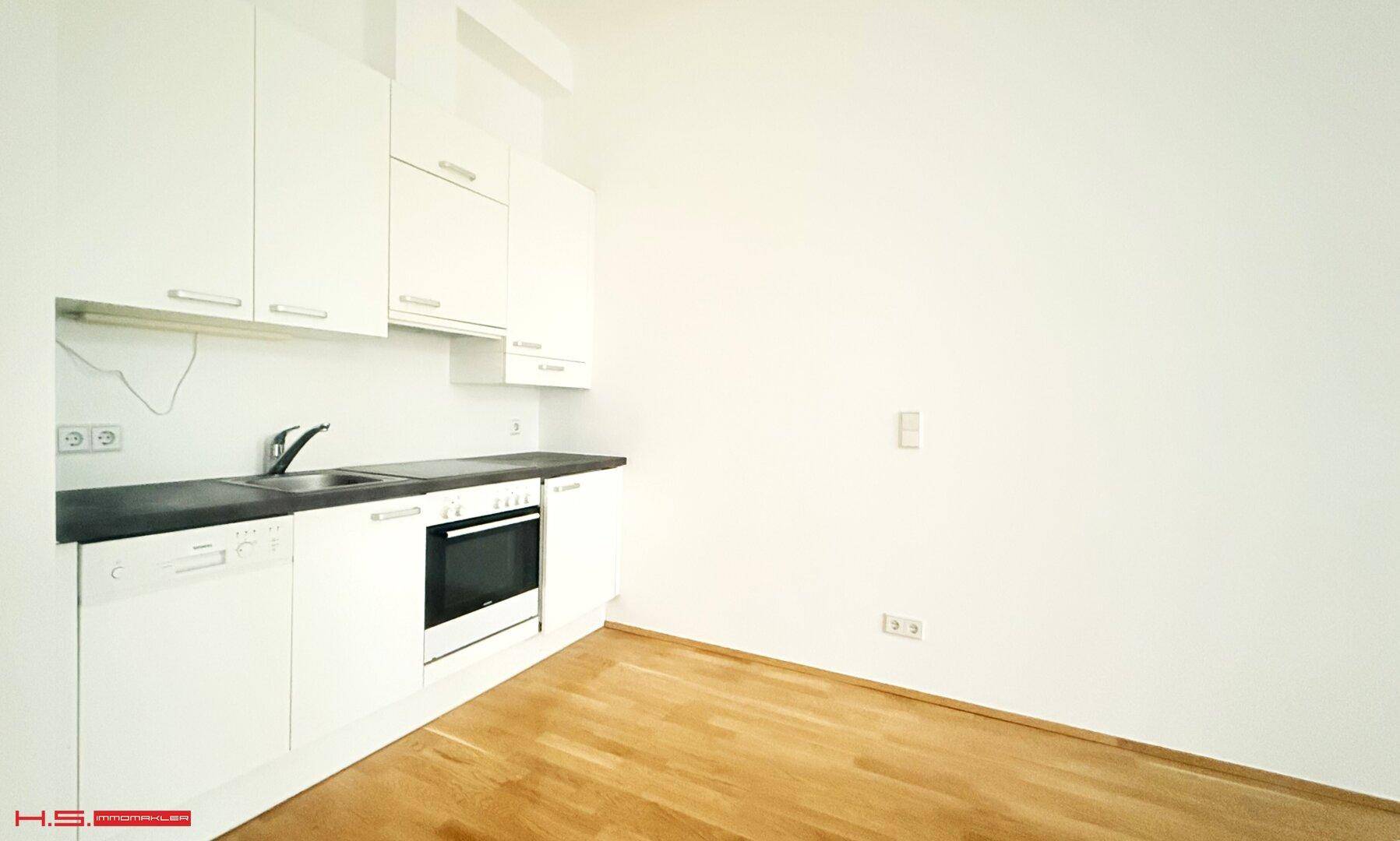 Moderne Küchenzeile mit weißen Schränken, dunkler Arbeitsplatte und integrierten Geräten.