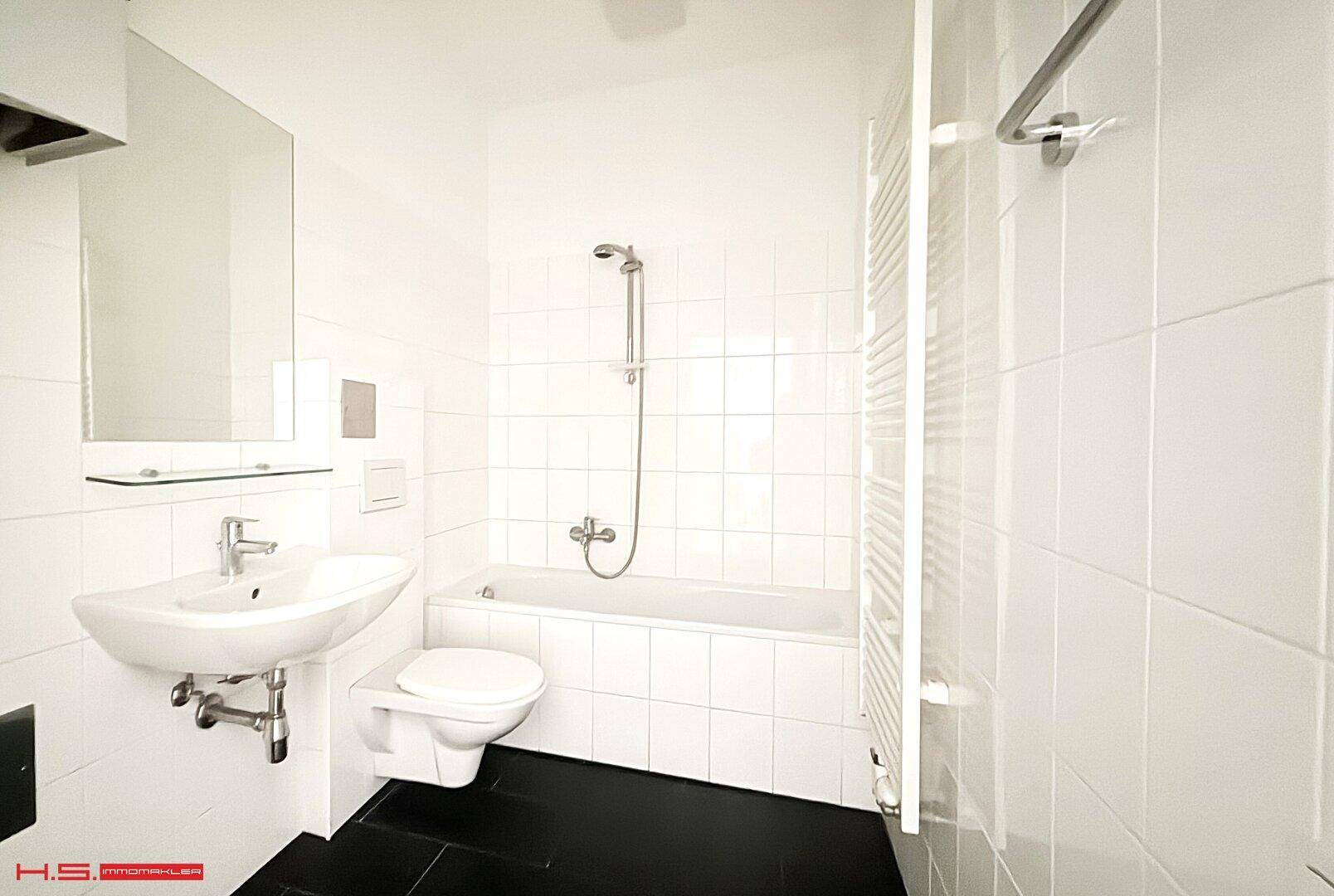 Modernes Badezimmer mit weißen Fliesen, Badewanne, WC und Waschbecken.