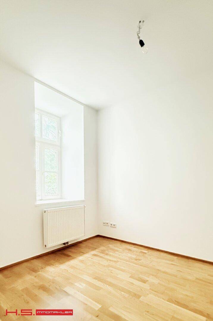 Freundliches Zimmer mit einem Fenster, weiß gestrichenen Wänden und Parkettboden.