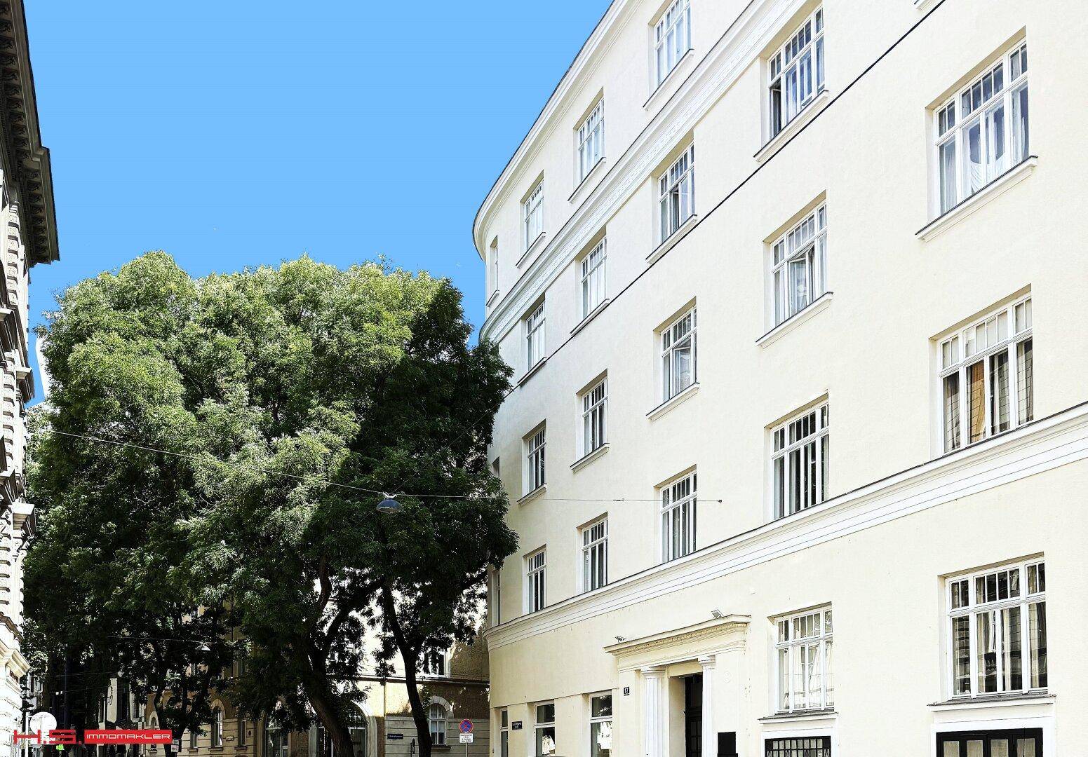 Elegante Fassade eines Mehrfamilienhauses mit vielen Fenstern und einem großen Baum davor.