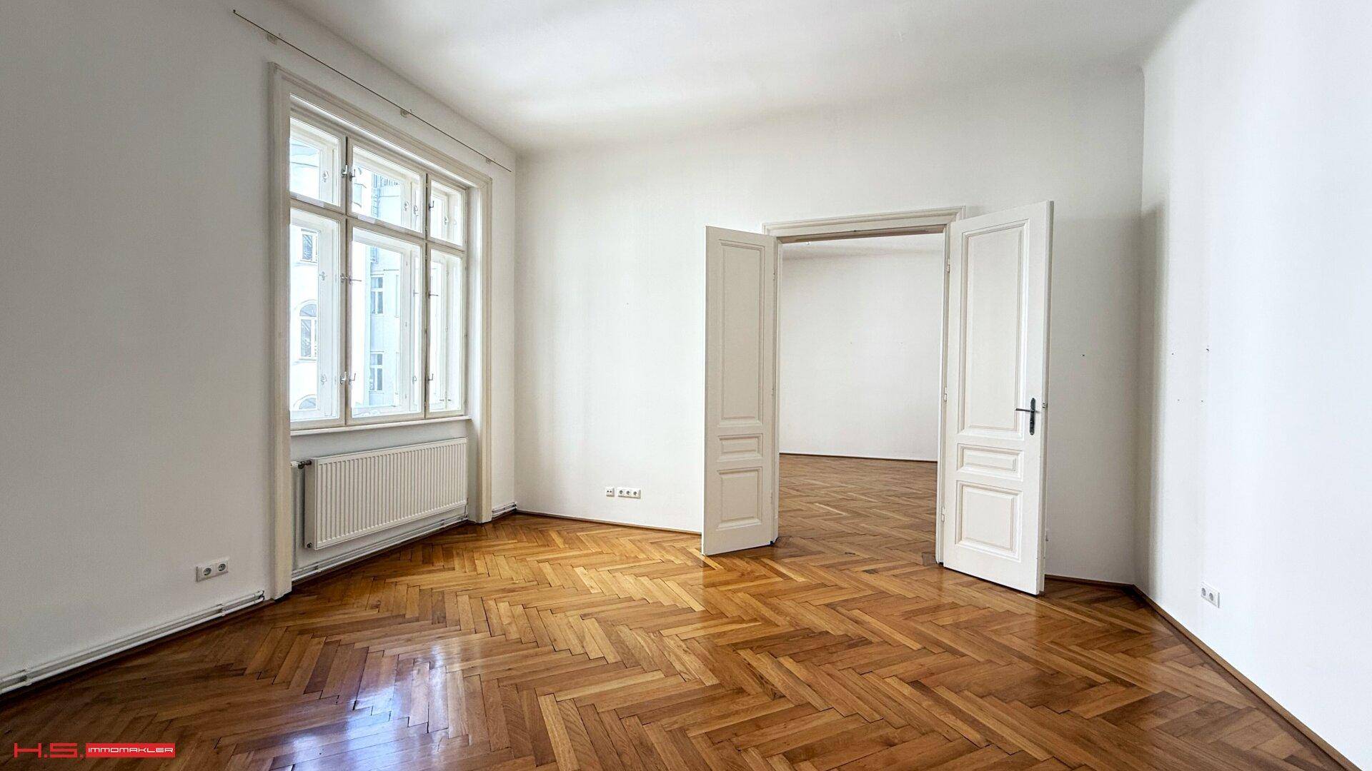 Geräumiges Zimmer mit Fischgrätparkett und großen Fenstern, die den Raum erhellen.