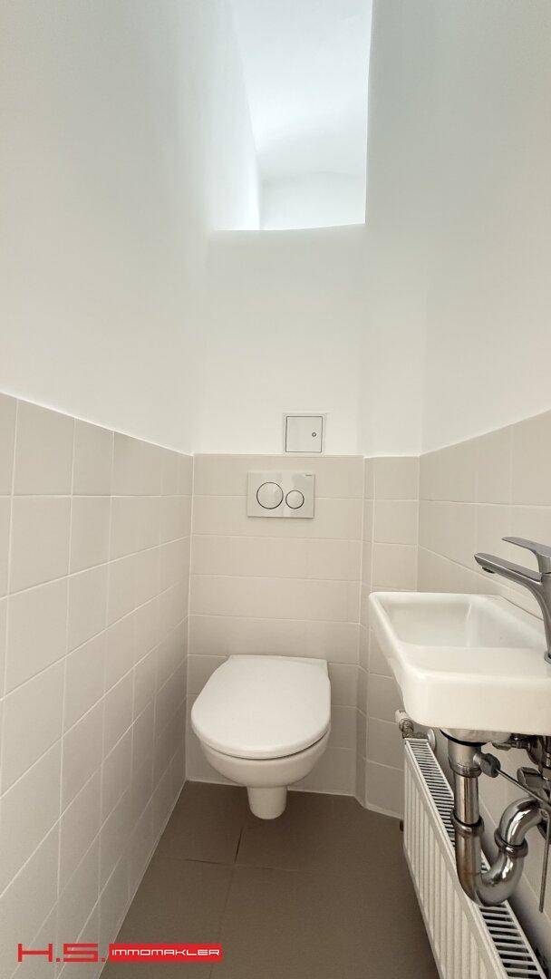 Modernes Gäste-WC mit Wand-WC, kleinem Waschbecken und hellen Fliesen.