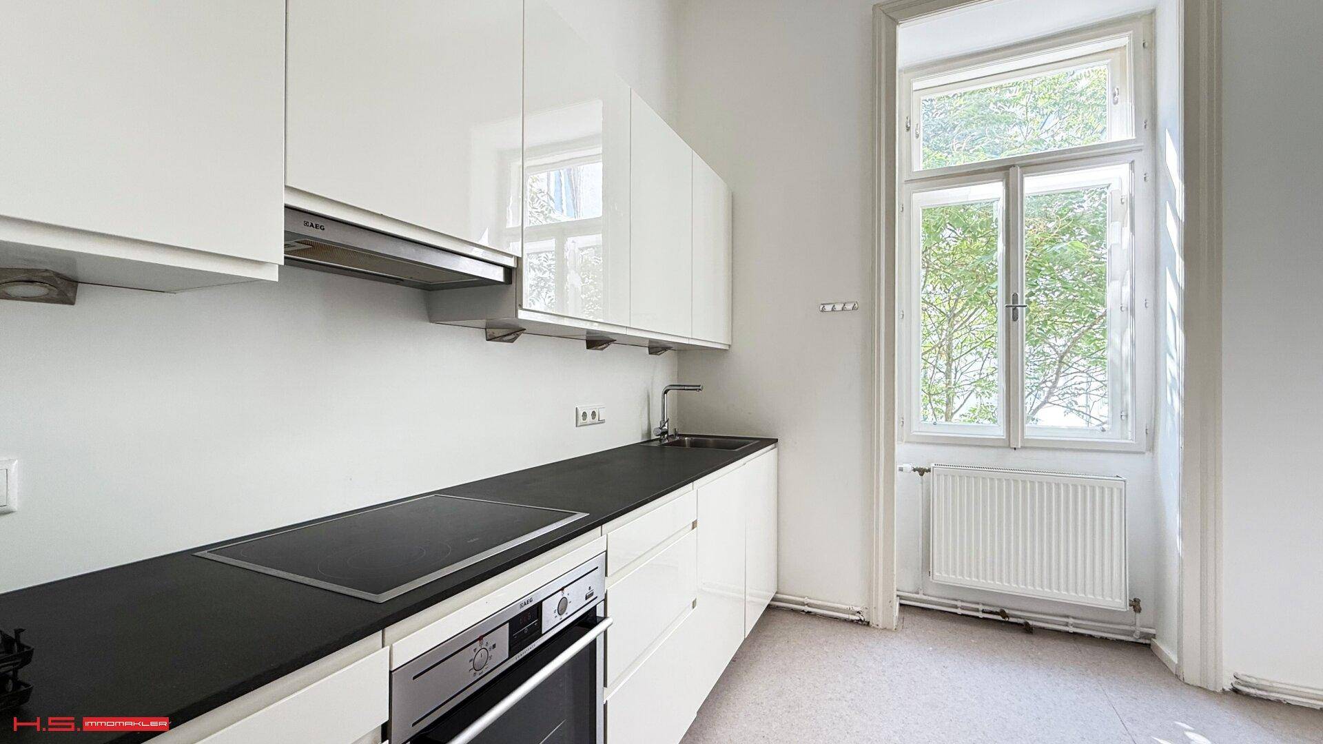 Moderne Küche mit weißen Hochglanzschränken, dunkler Arbeitsplatte und großem Fenster.