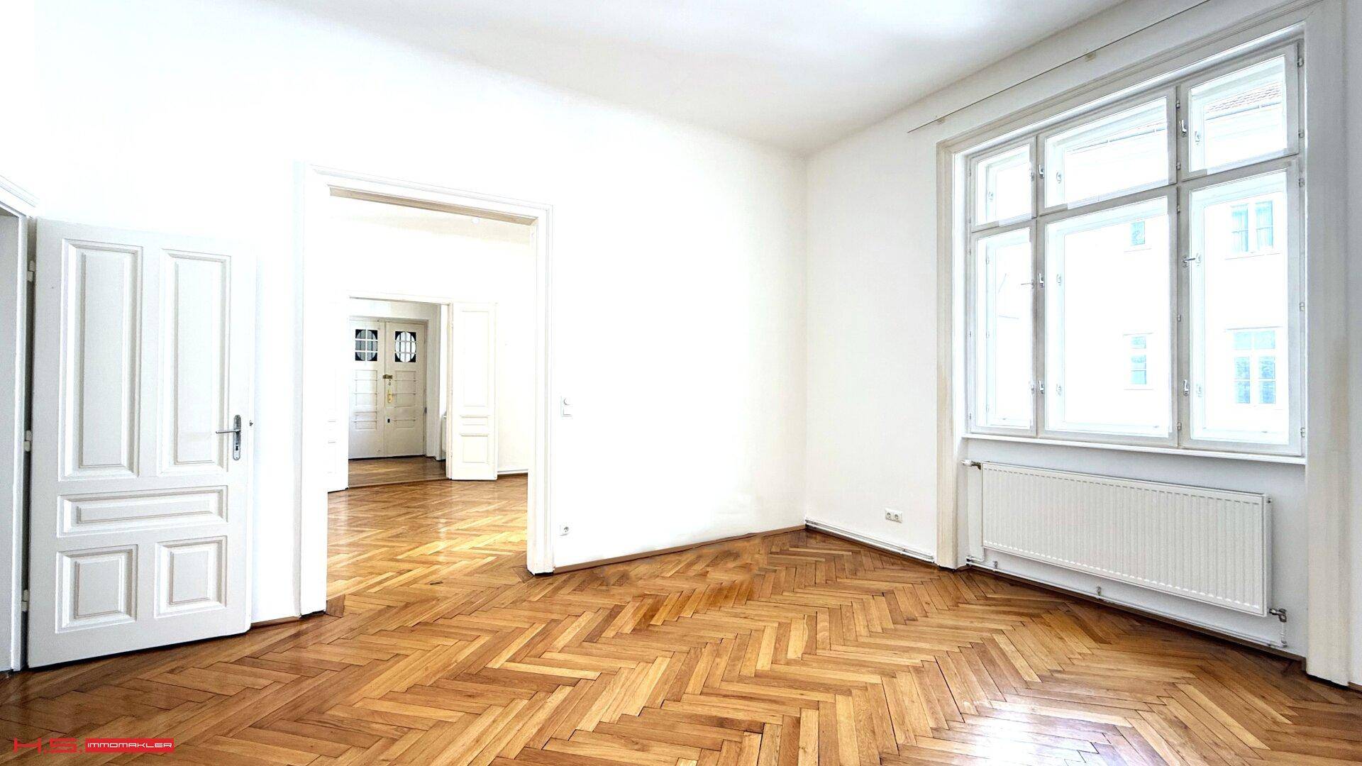 Helles Zimmer mit Fischgrätparkett und hohen weißen Türen, das viel Tageslicht erhält.