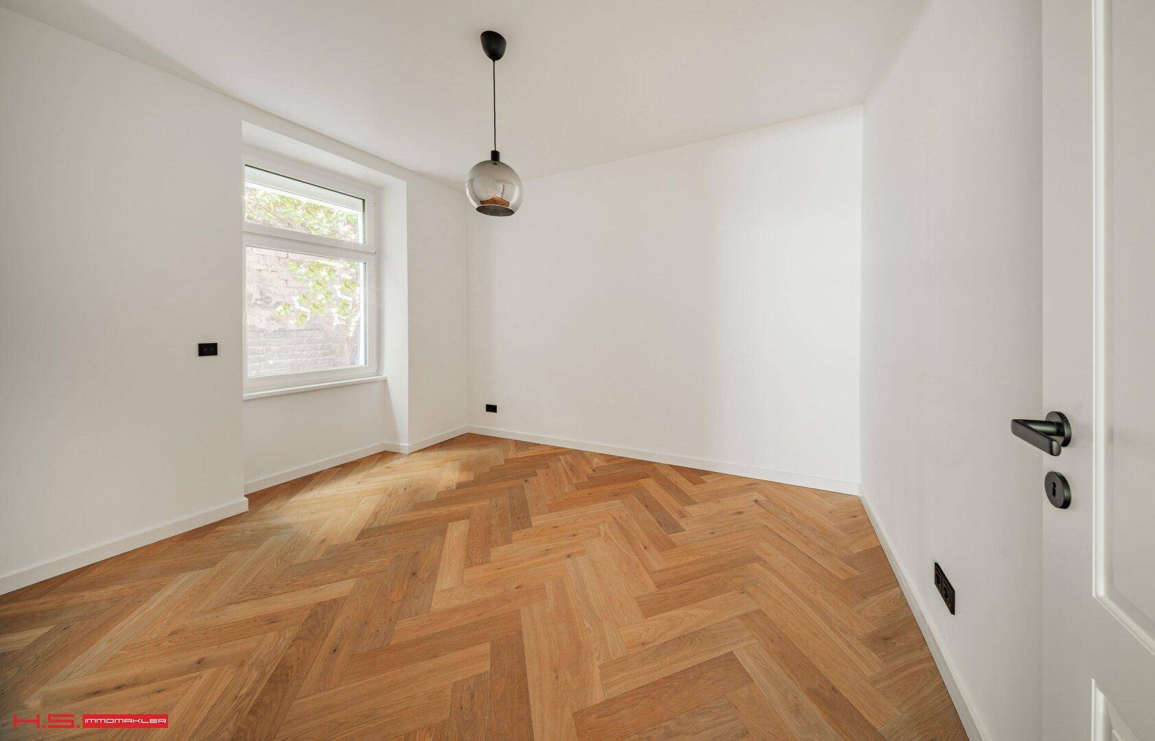 Ruhiges Schlafzimmer mit Fischgrätparkett und einem Fenster, das viel Licht hereinlässt.