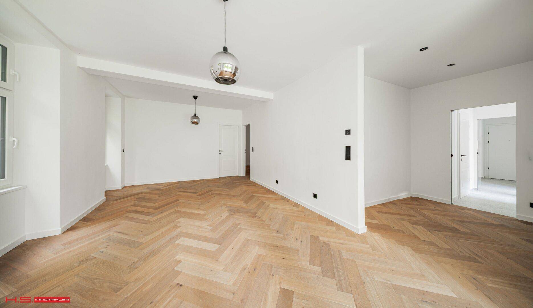 Geräumiger, heller Raum mit elegantem Fischgrätparkett und weißen Wänden.