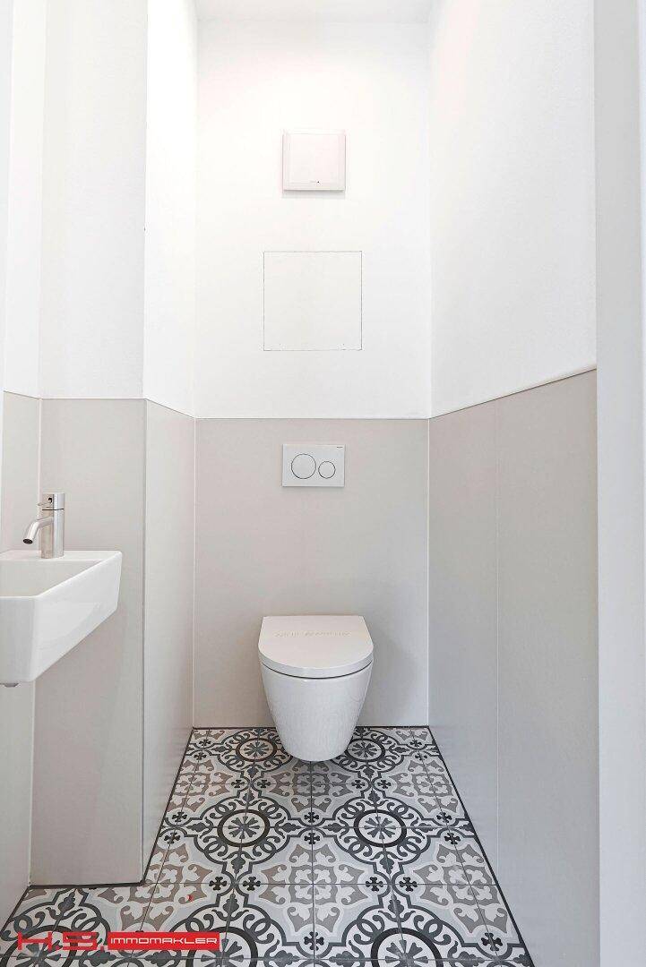 Modernes Gäste-WC mit wandhängender Toilette, kleinem Waschbecken und dekorativen Bodenfliesen.