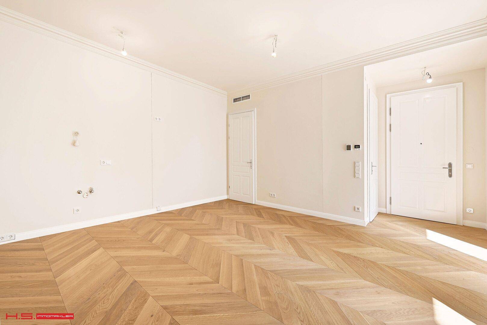 Heller Raum mit elegantem Fischgrätparkett, weißen Wänden und klassischer Stuckverzierung an der Decke.