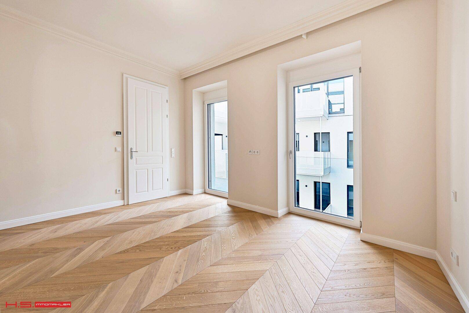 Heller Wohnraum mit Fischgrätparkett und großen Fenstertüren, die einen Blick auf die moderne Architektur bieten.