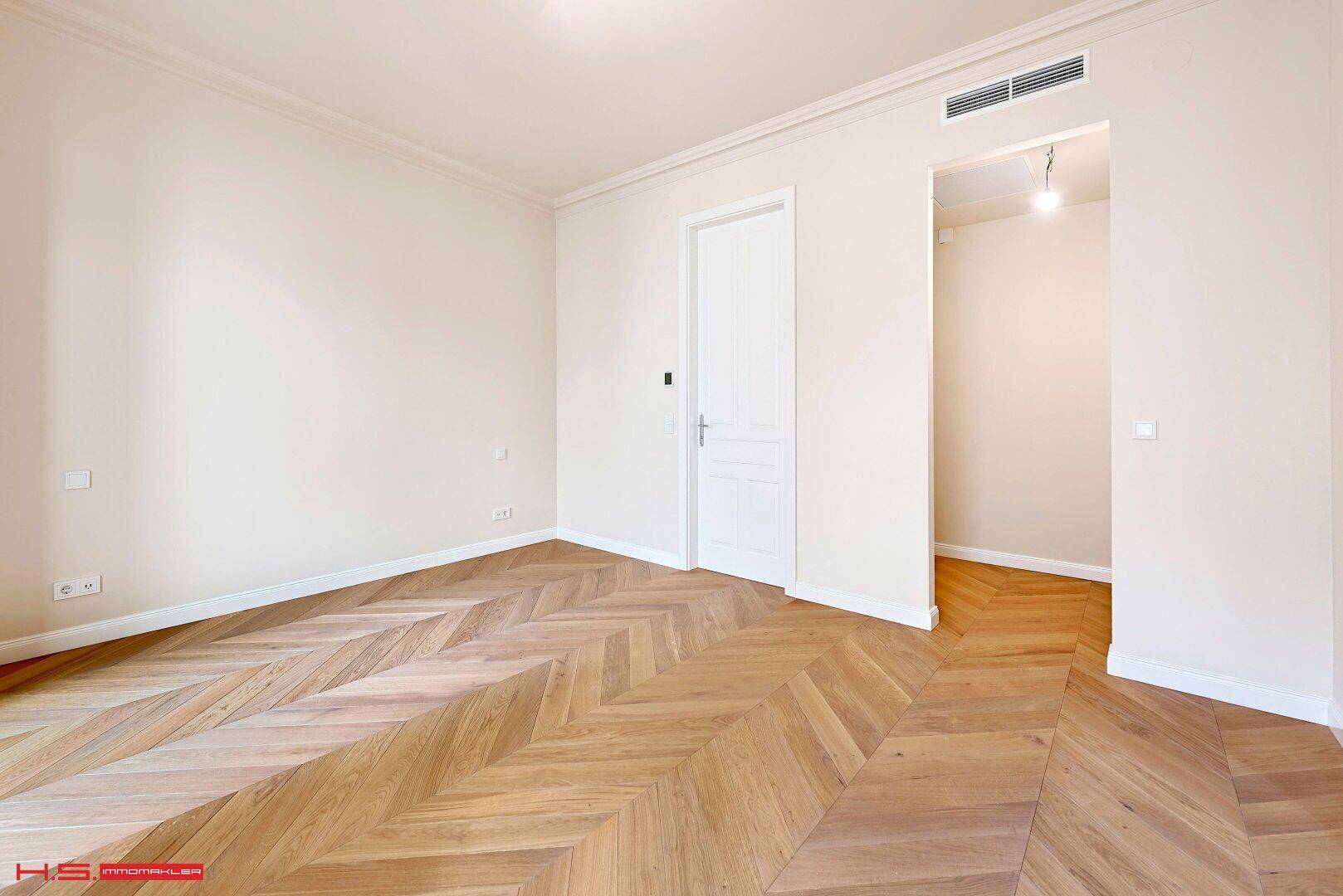 Heller Wohnraum mit Fischgrätparkett, weißen Türen und einem Übergang zu einem weiteren Zimmer.