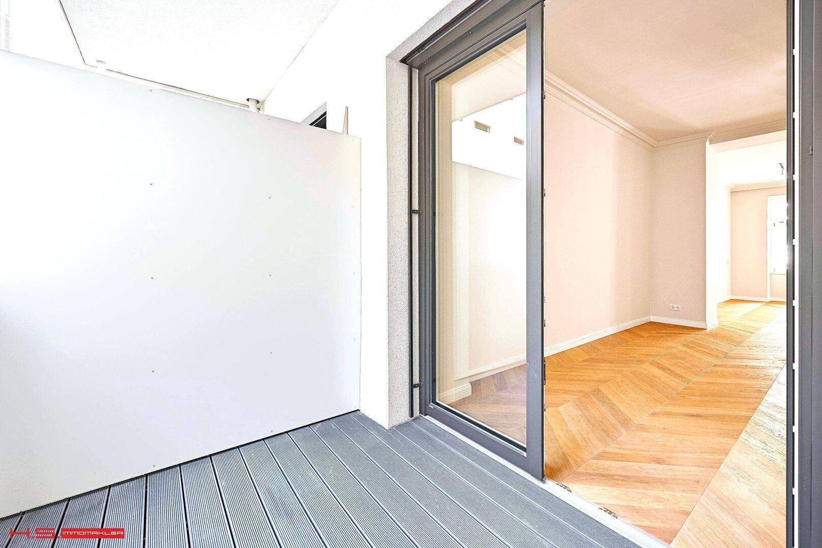 Heller Balkon mit Holzdielenboden und Blick in den angrenzenden Wohnbereich.