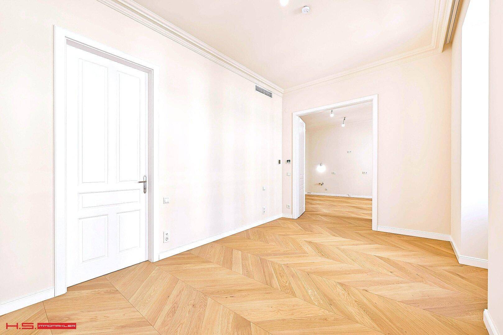 Helles Zimmer mit Fischgrätparkett und Zugang zu weiteren Räumen, ideal als Schlafzimmer.