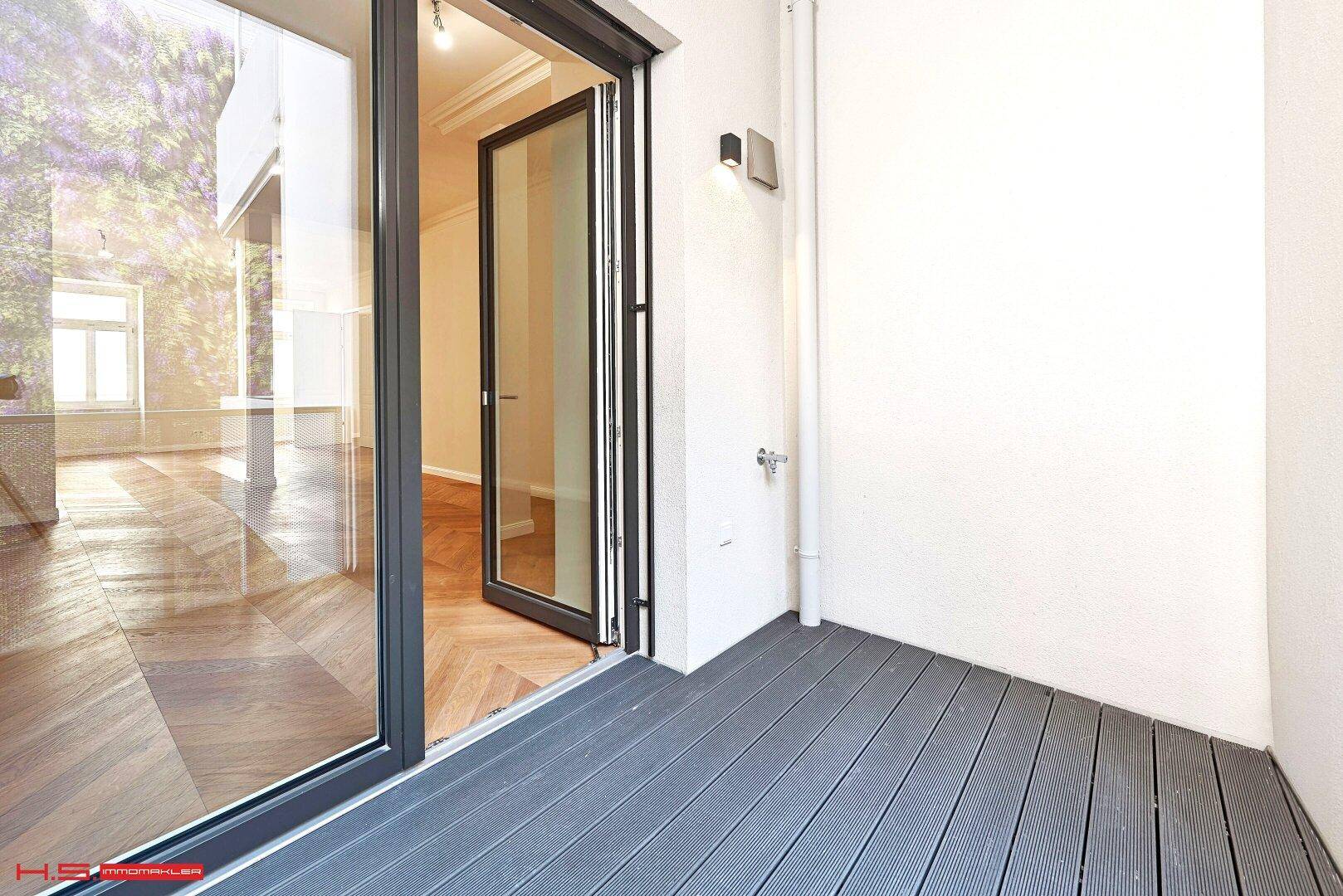 Kleiner Balkon mit Holzdielenboden und Zugang zu einem hellen Innenraum.