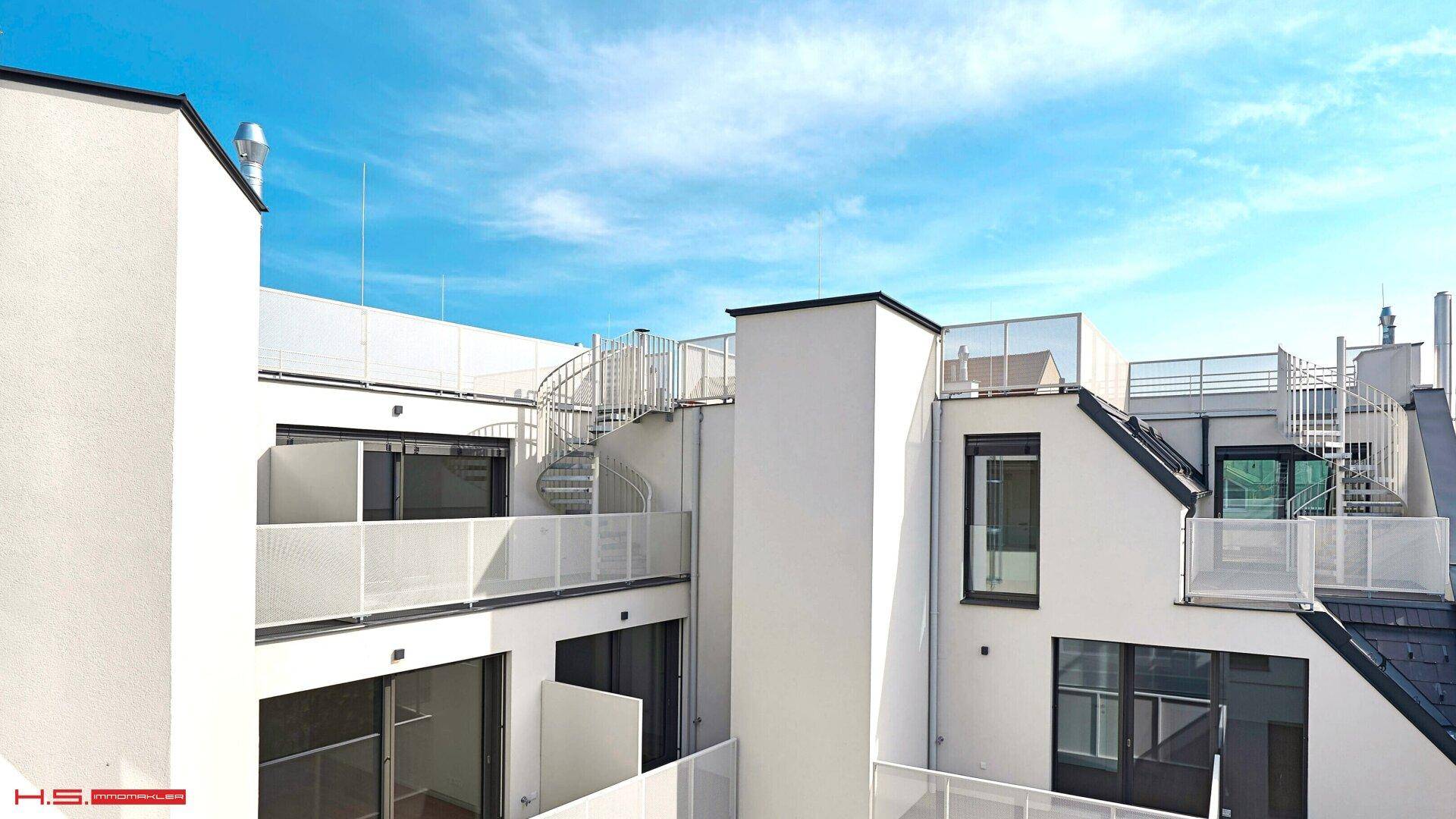 Moderne Architektur mit weißen Fassaden, Balkonen und einer Wendeltreppe zum Dach.