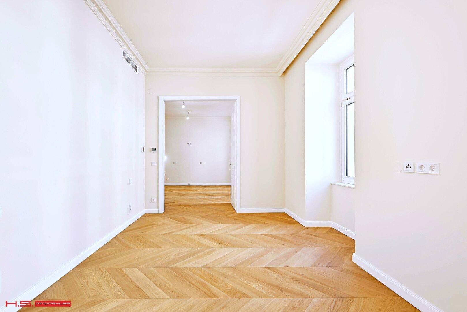 Helles Zimmer mit Fischgrätparkett und Zugang zu weiteren Räumen, ideal für flexible Nutzung.