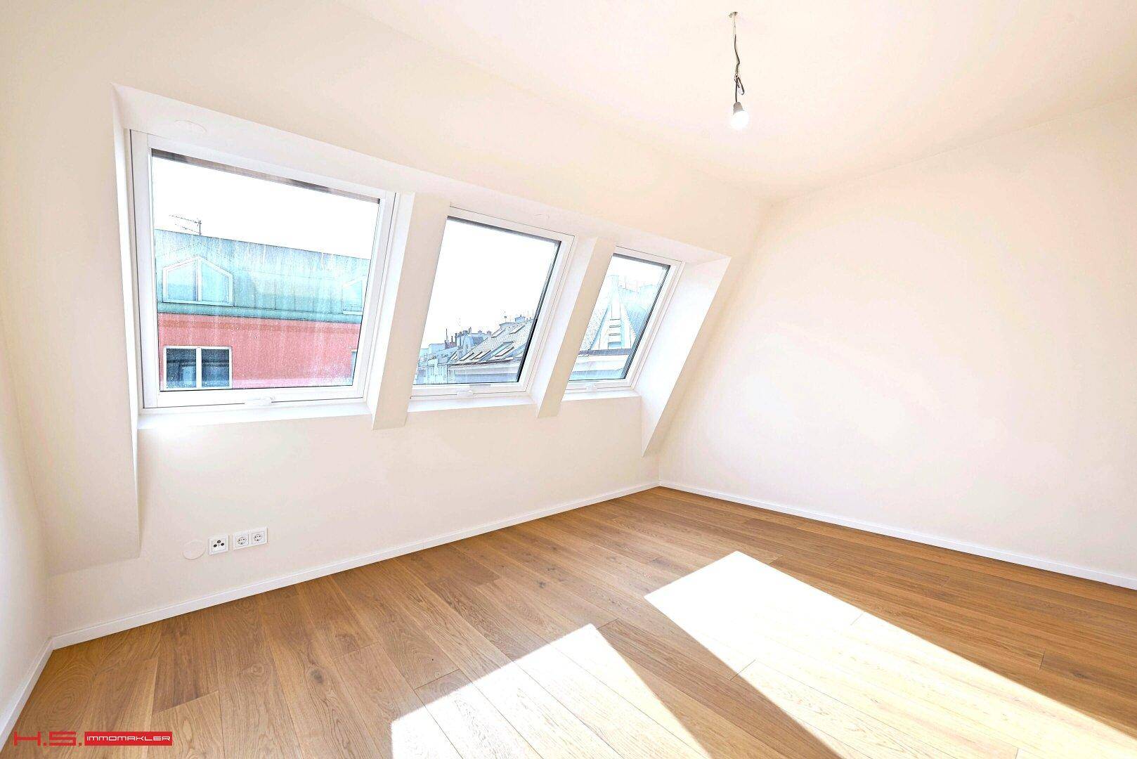 Helles Schlafzimmer mit Holzboden und Dachfenstern, die viel Sonnenlicht hereinlassen.