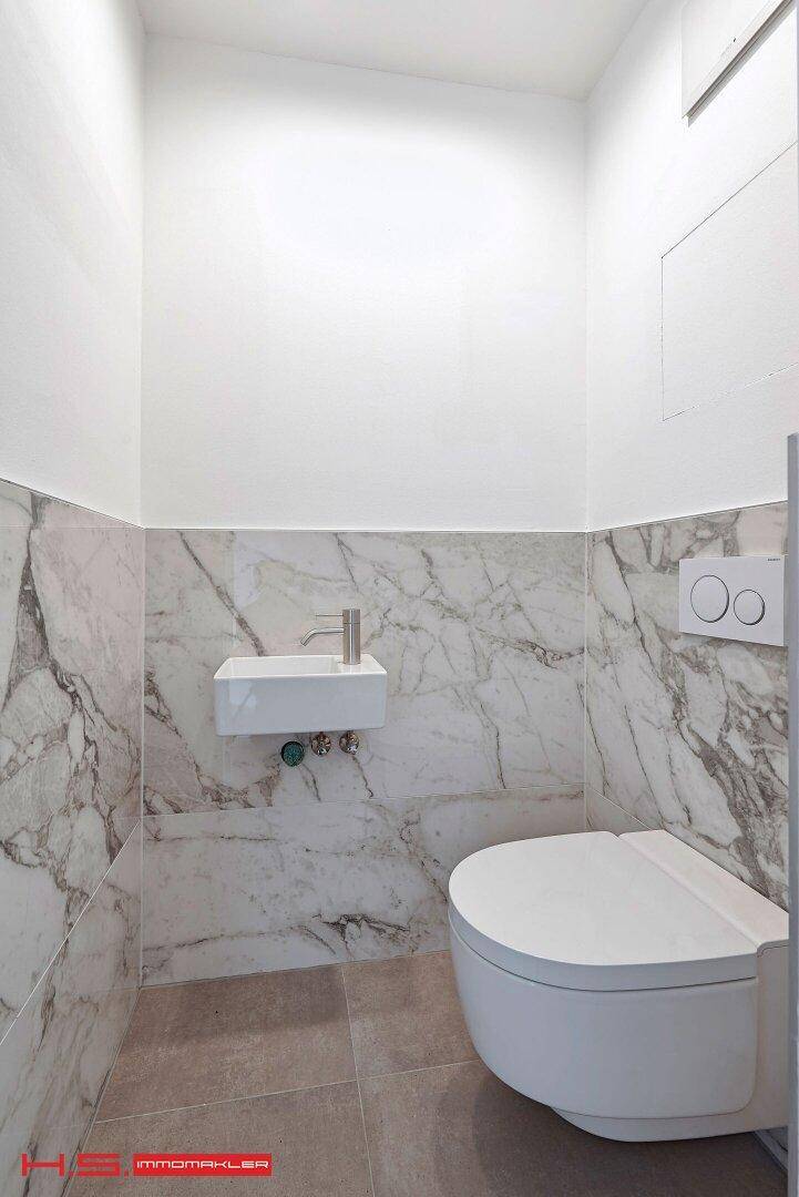 Modernes Gäste-WC mit Marmorfliesen, wandhängendem WC und kleinem Waschbecken.