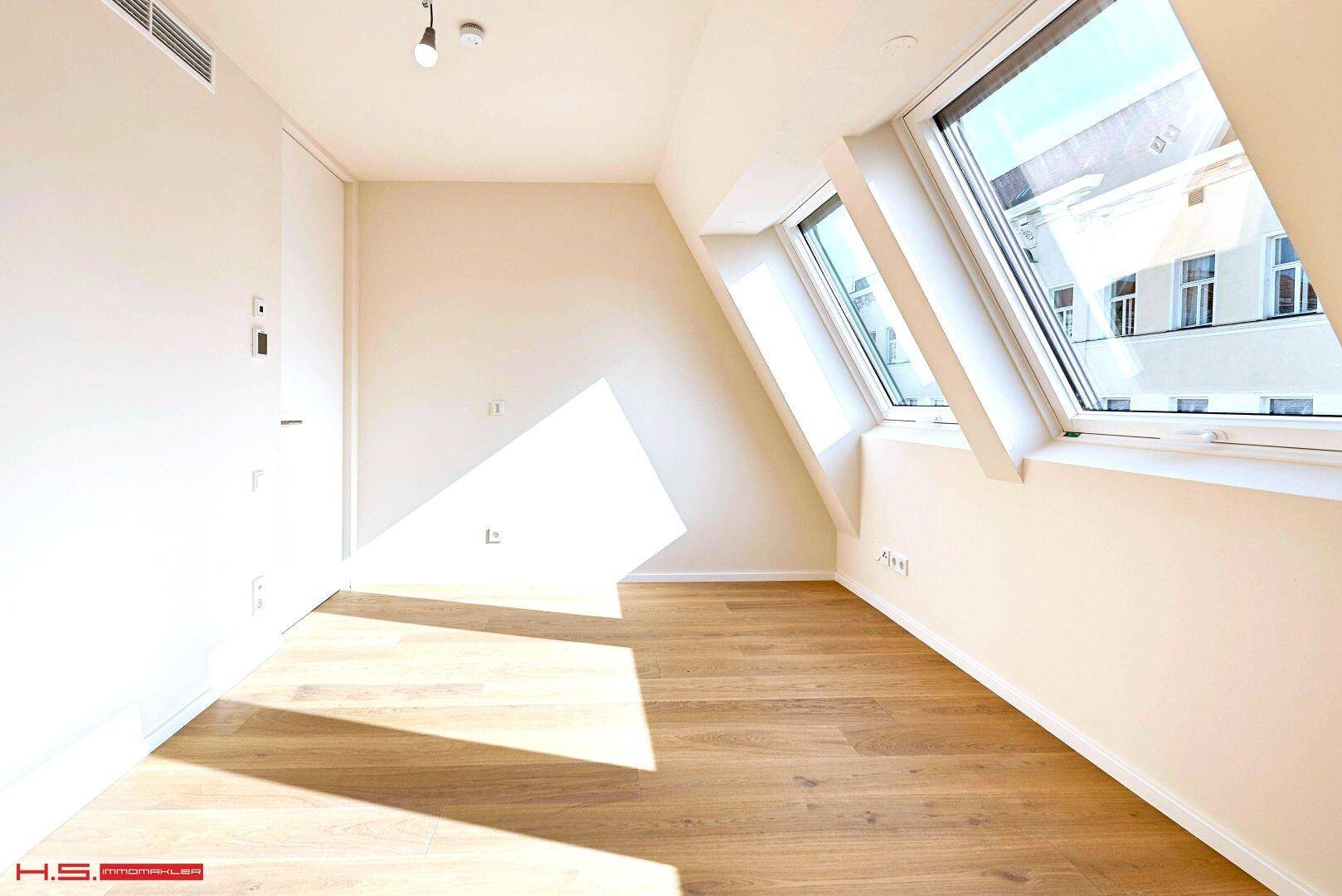 Lichtdurchflutetes Schlafzimmer mit Holzboden und Dachfenstern, die eine helle Atmosphäre schaffen.