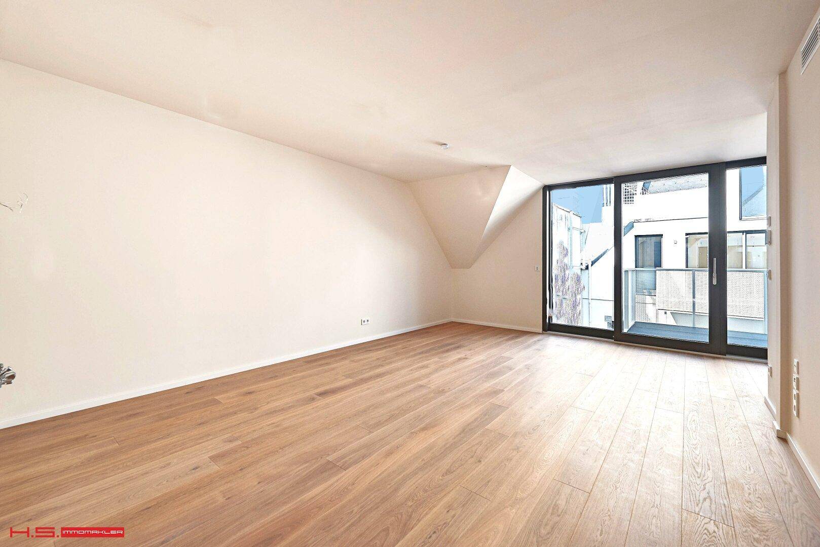 Heller, leerer Raum mit Holzboden und großen Fenstern, die viel Tageslicht hereinlassen.