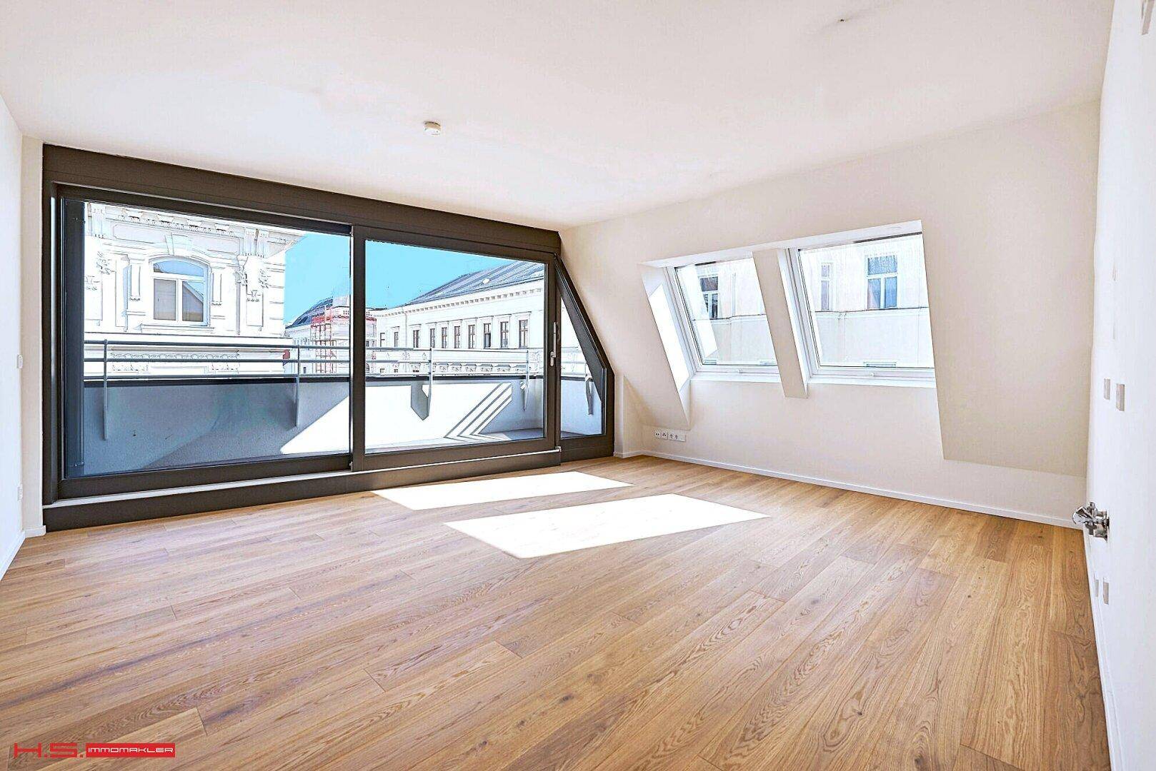 Heller Raum mit Holzboden, großen Schiebetüren zum Balkon und Dachfenstern für viel Tageslicht.