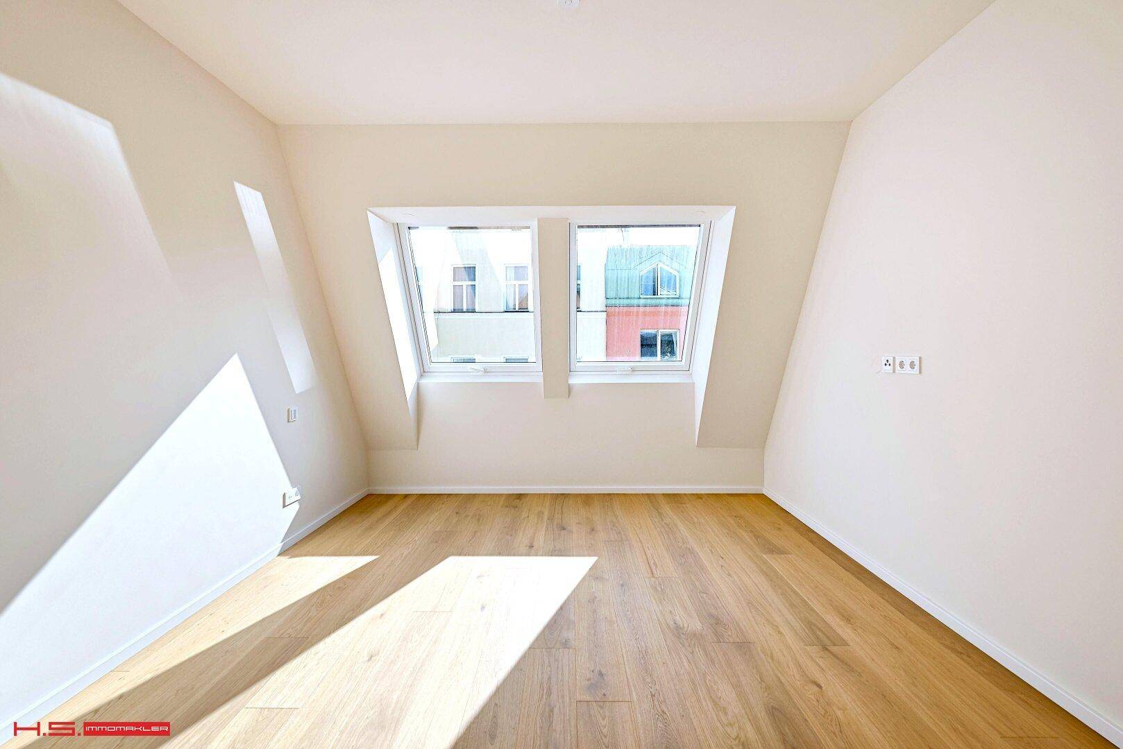 Leerer Raum mit Holzboden und zwei Dachfenstern, die für eine helle und freundliche Atmosphäre sorgen.