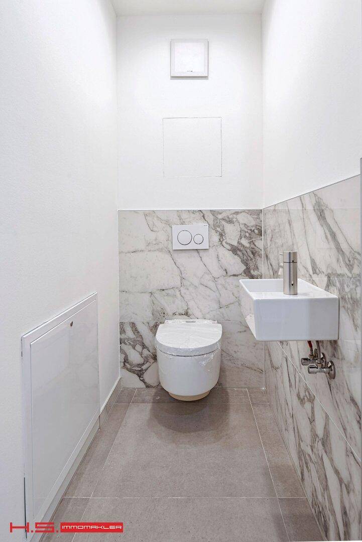 Modernes Gäste-WC mit Marmorfliesen, wandhängender Toilette und kleinem, stilvollem Waschbecken.