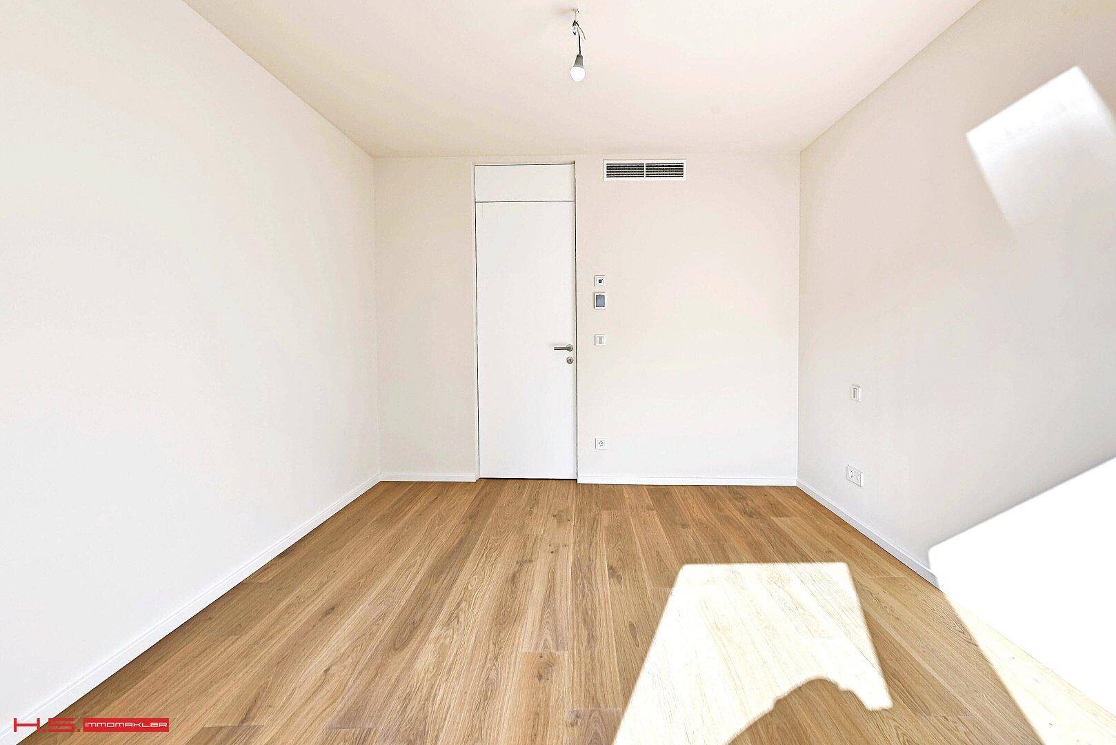 Heller, leerer Raum mit Holzboden, weißen Wänden und integrierter Klimaanlage.