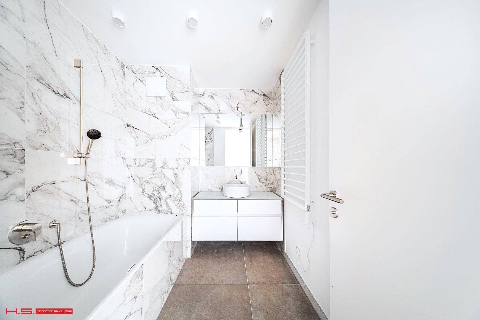 Modernes Badezimmer mit eleganten Marmorfliesen, Badewanne und einem stilvollen Waschtisch.