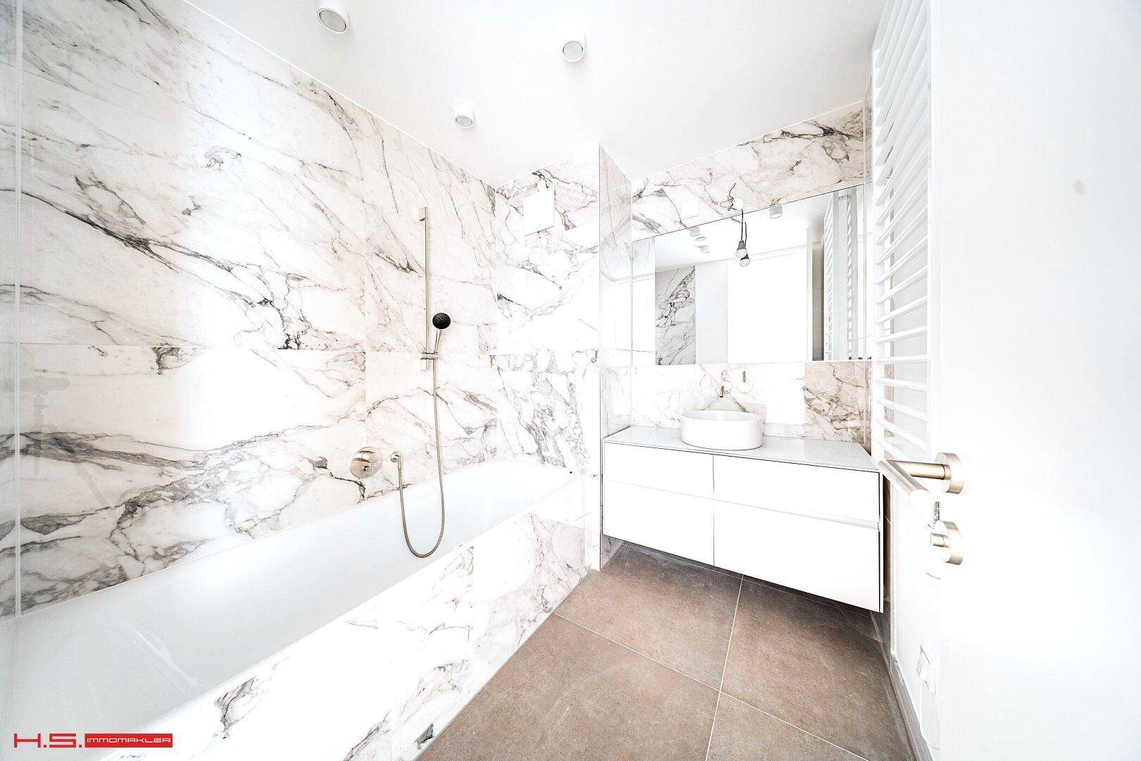 Modernes Badezimmer mit eleganten Marmorfliesen, Badewanne und einem stilvollen Waschtisch.