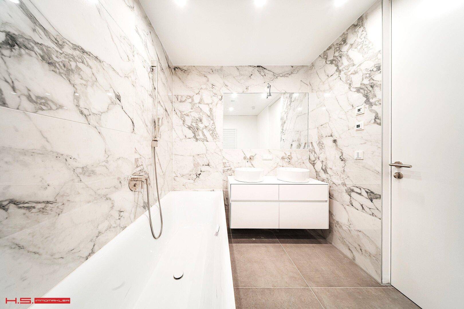 Elegantes Badezimmer mit Marmorfliesen, Doppelwaschbecken und moderner Badewanne.
