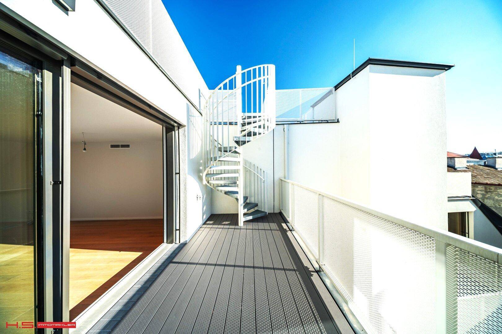 Balkon mit moderner Wendeltreppe, die zu einer weiteren Ebene führt, und Blick auf die Umgebung.