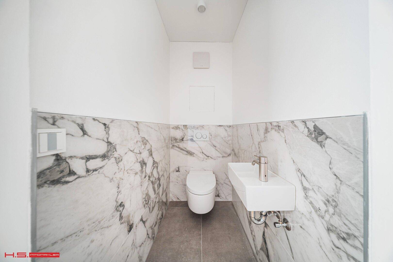 Modernes Gäste-WC mit Marmorfliesen, wandhängender Toilette und kleinem Waschbecken.