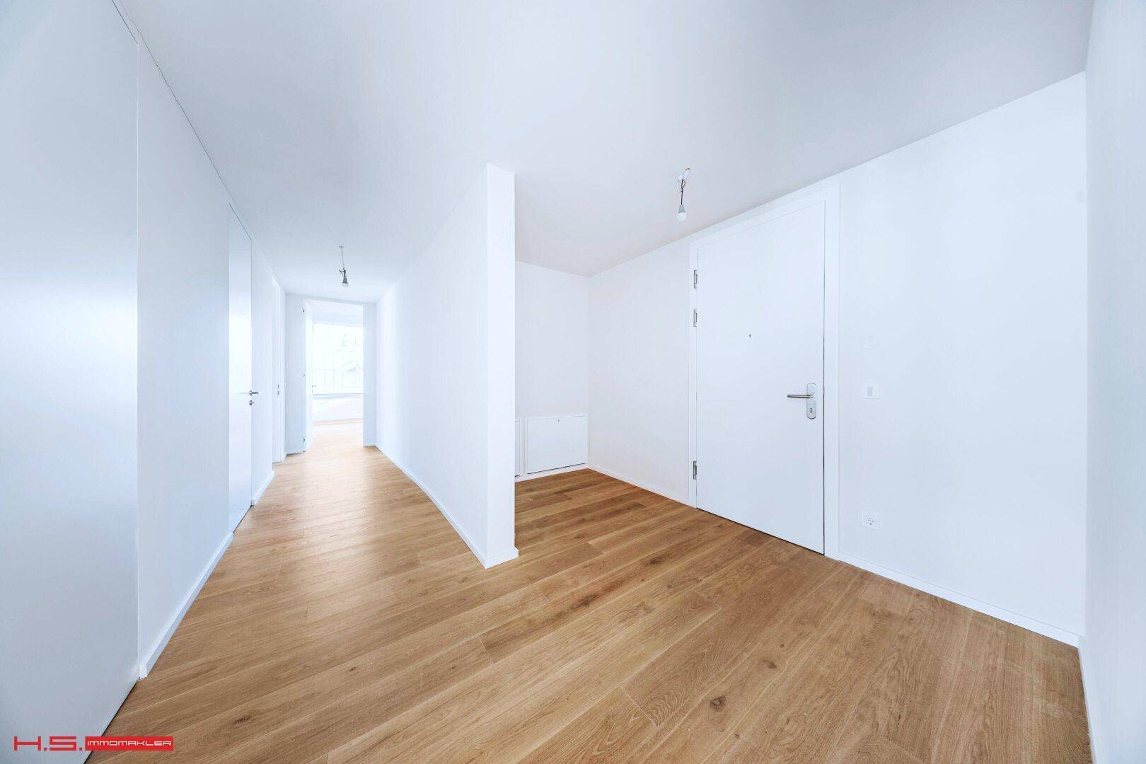 Langer, heller Flur mit Holzboden und weißen Wänden, der zu weiteren Räumen führt.