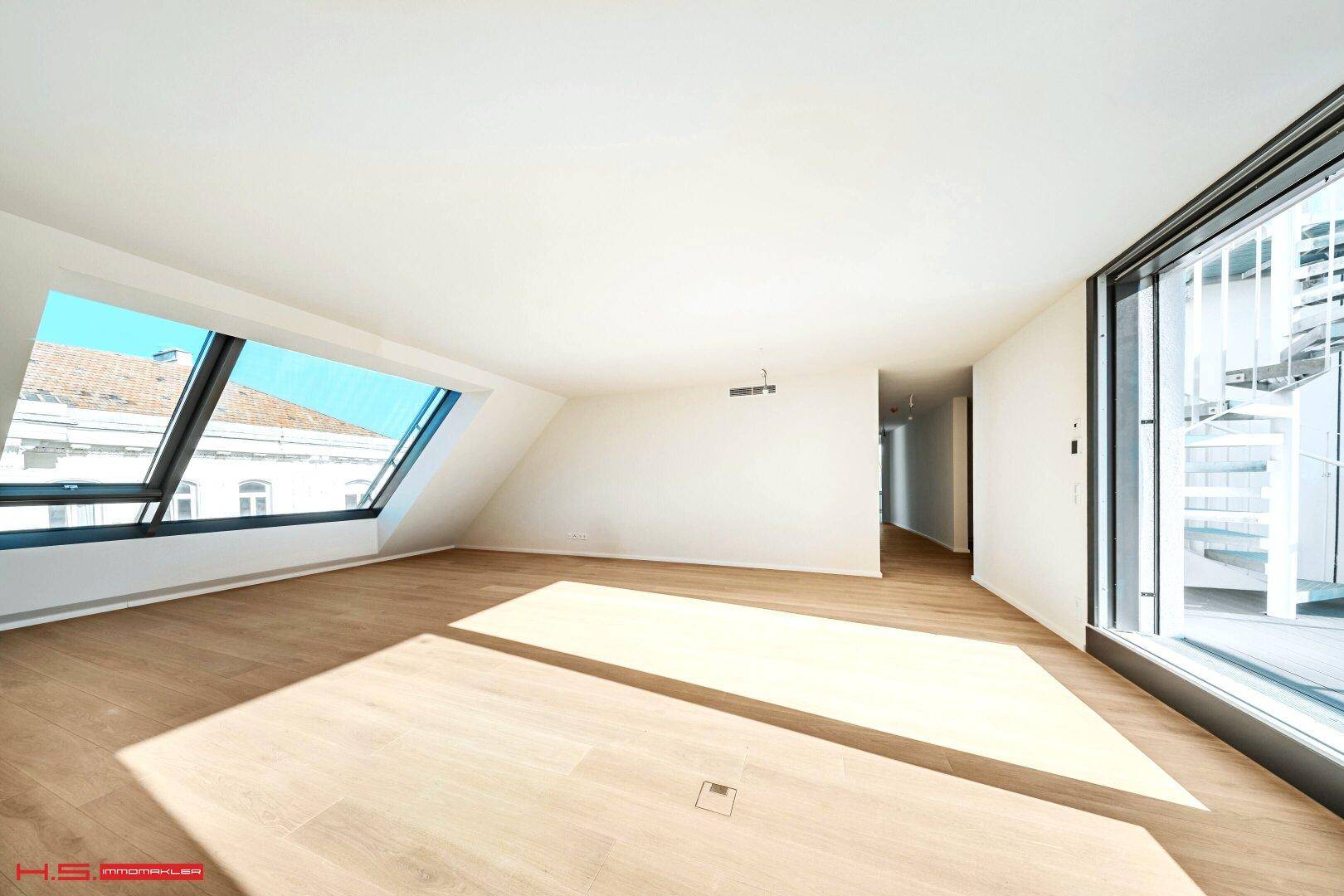 Geräumiger, heller Raum mit Holzboden und großen Fenstern, die viel Tageslicht hereinlassen.