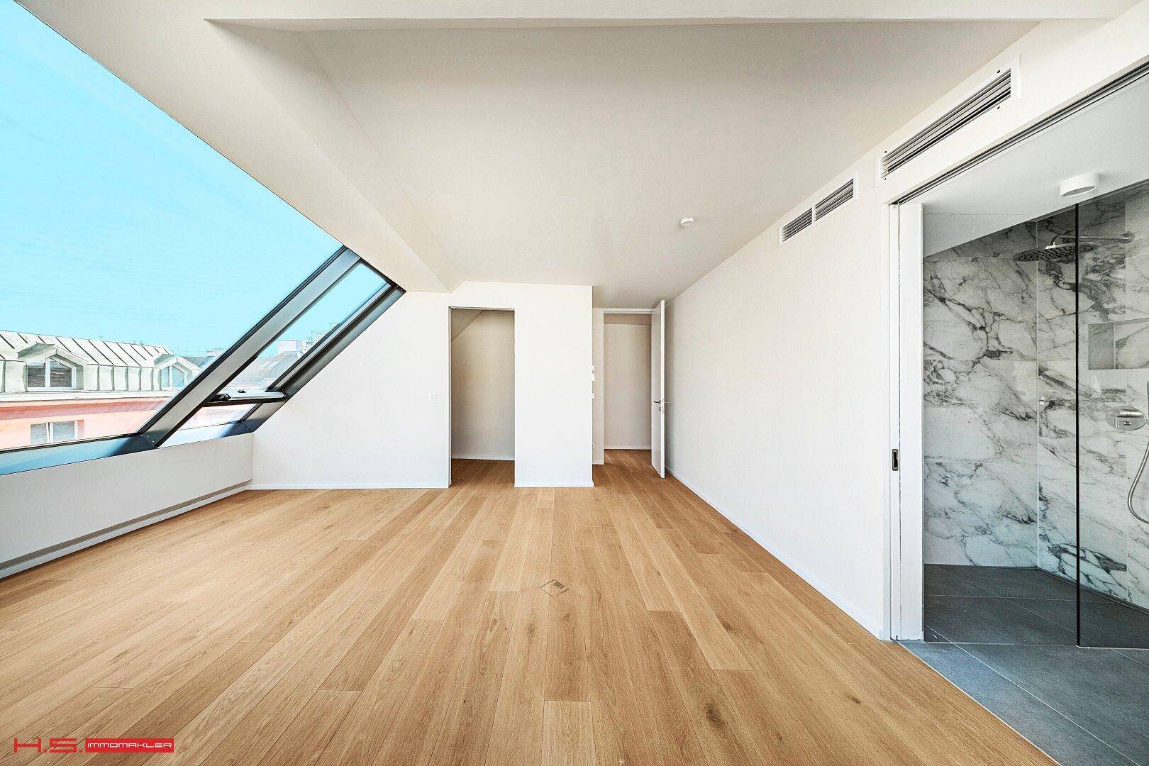 Heller Raum mit Holzboden, großen Dachfenstern und direktem Zugang zu einem Badezimmer.