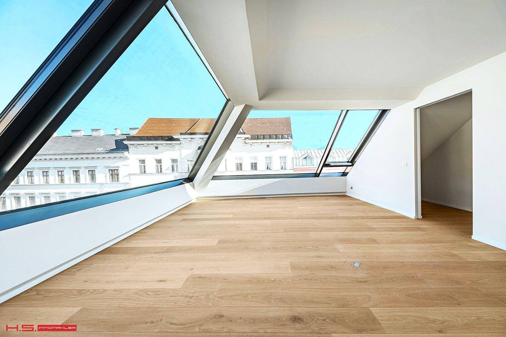 Geräumiger, heller Raum mit Holzboden und großen Dachfenstern, die eine weite Aussicht bieten.