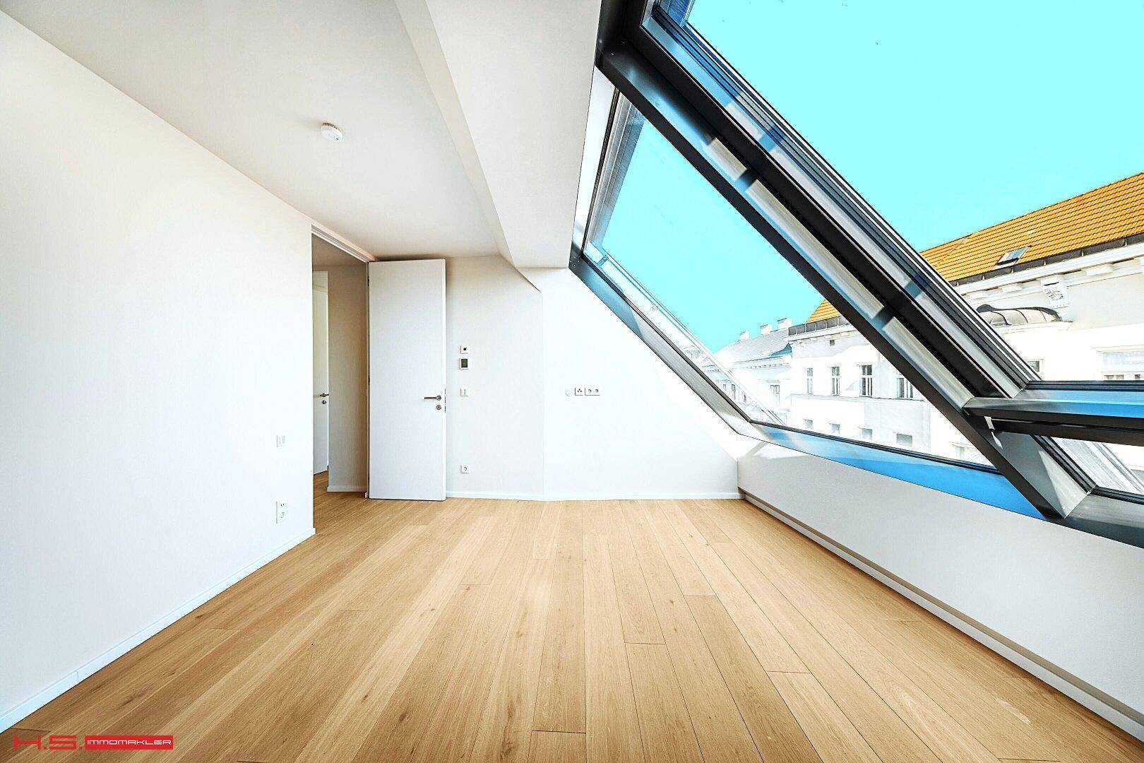 Lichtdurchfluteter Raum mit Holzboden und großen Dachfenstern, die einen urbanen Blick bieten.