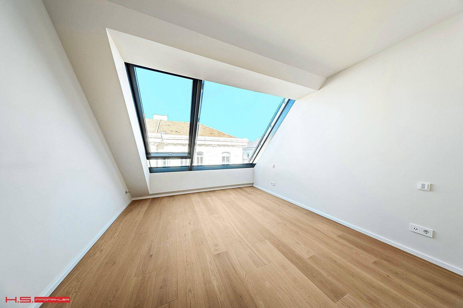 Kleiner, heller Raum mit Holzboden und einem großen Dachfenster, das Tageslicht spendet.