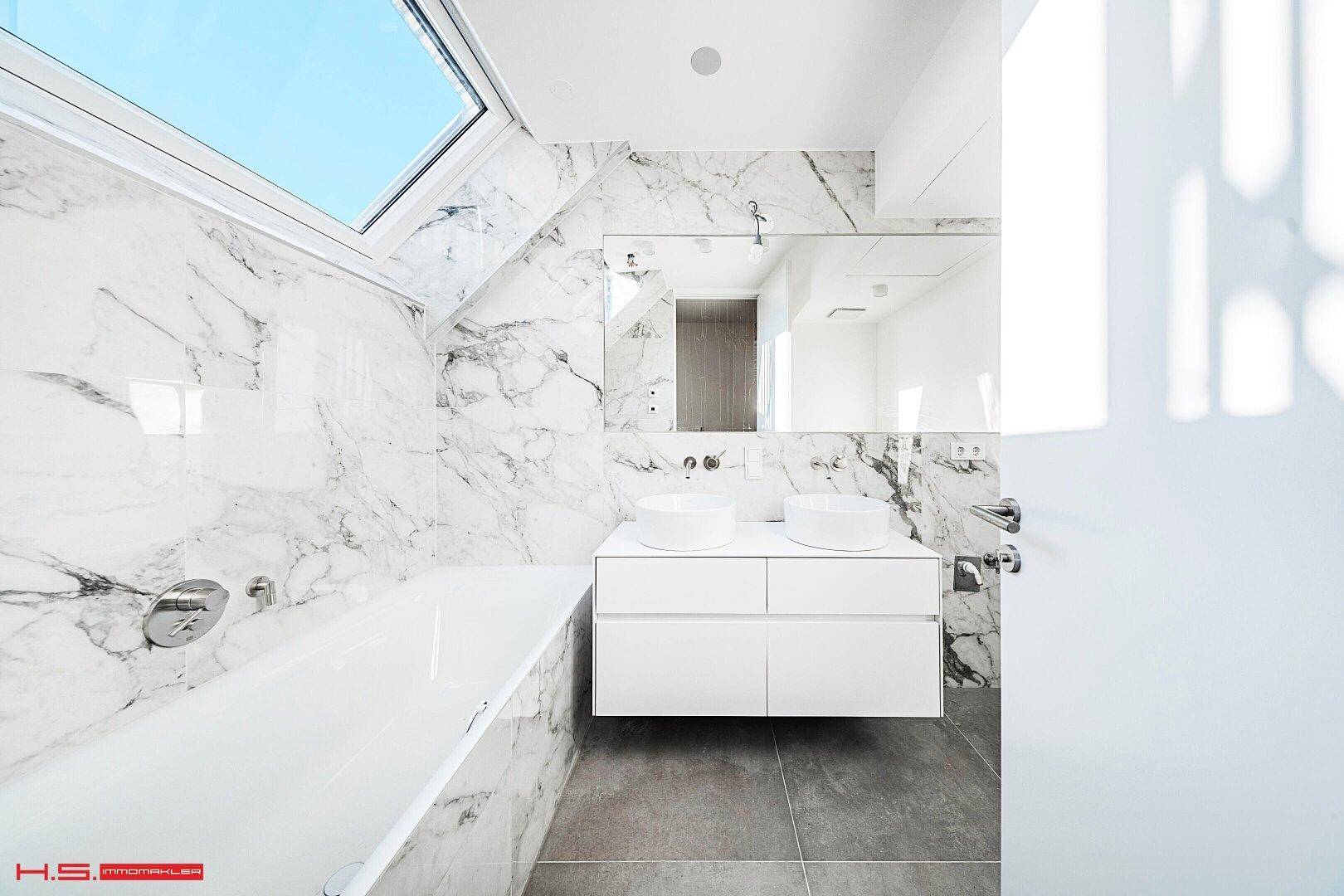 Modernes Badezimmer mit Marmorfliesen, Doppelwaschbecken und Badewanne unter einem Dachfenster.