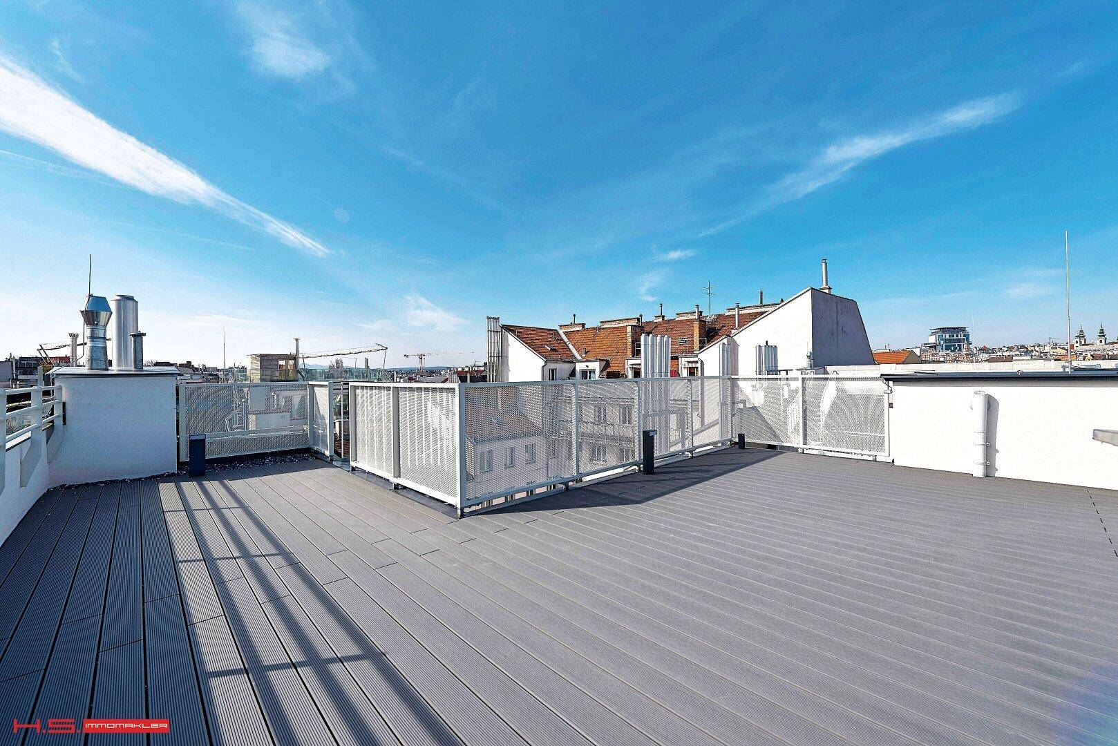 Weitläufige Dachterrasse mit Blick auf die umliegenden Gebäude und den Himmel.