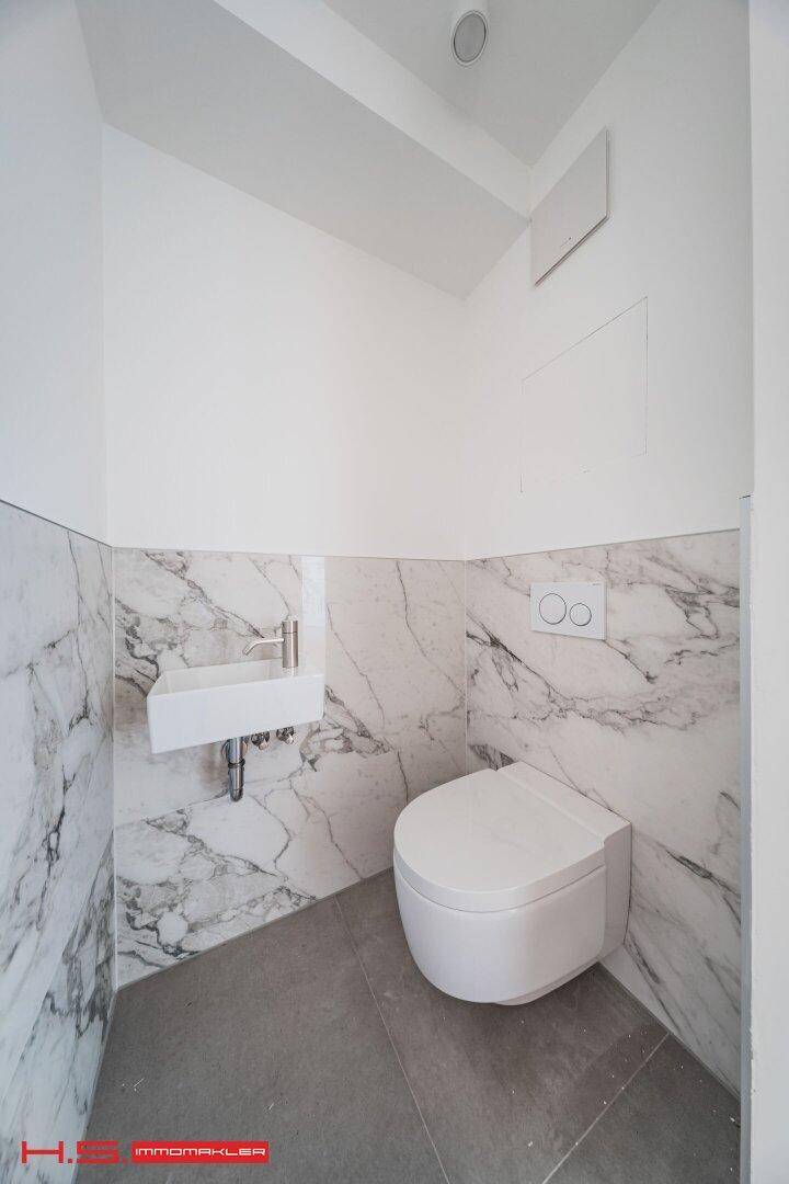 Modernes Gäste-WC mit Marmorfliesen, wandhängender Toilette und kleinem Waschbecken.