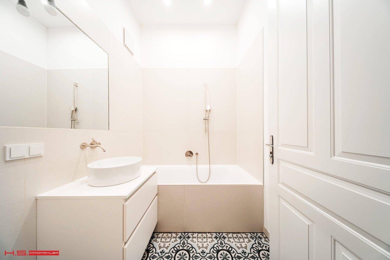 Helles Badezimmer mit Badewanne, modernem Waschtisch und dekorativen Bodenfliesen.