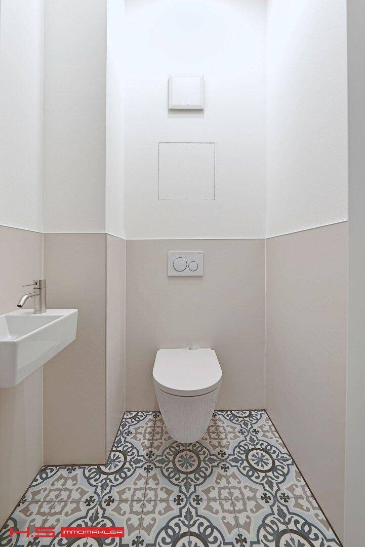 Modernes Gäste-WC mit Wand-WC, kleinem Waschbecken und gemusterten Bodenfliesen.