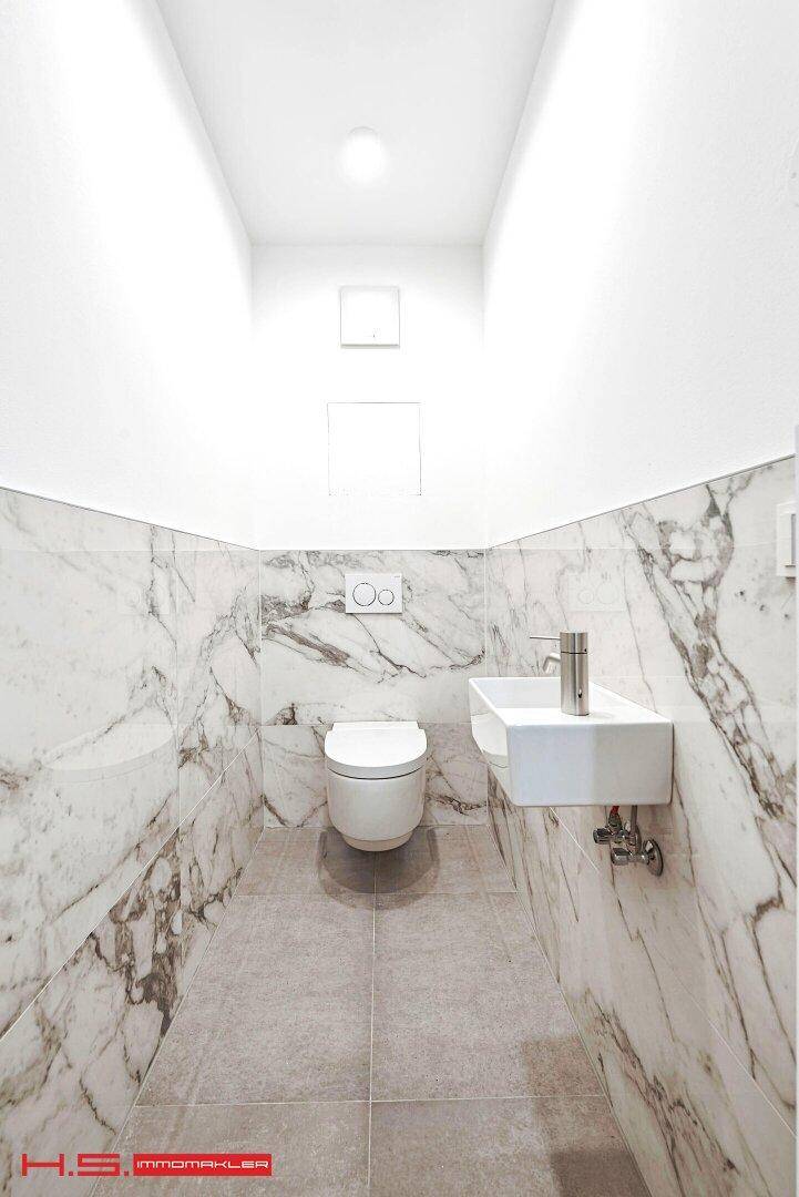 Modernes Gäste-WC mit Marmorverkleidung, wandhängender Toilette und kleinem Waschbecken.