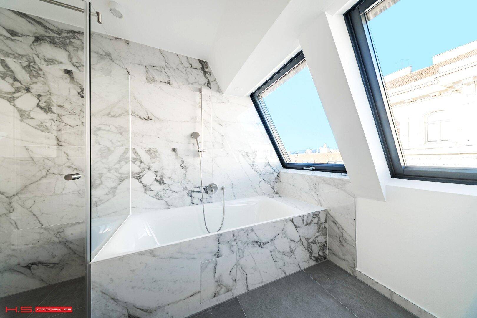 Elegantes Badezimmer mit Marmorverkleidung, integrierter Badewanne und begehbarer Dusche unter Dachfenstern.