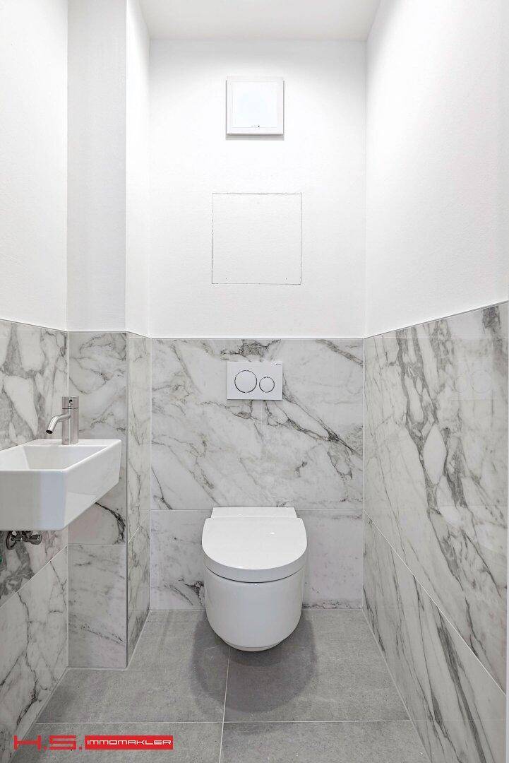 Modernes Gäste-WC mit Marmorfliesen, wandmontierter Toilette und kleinem Waschbecken.
