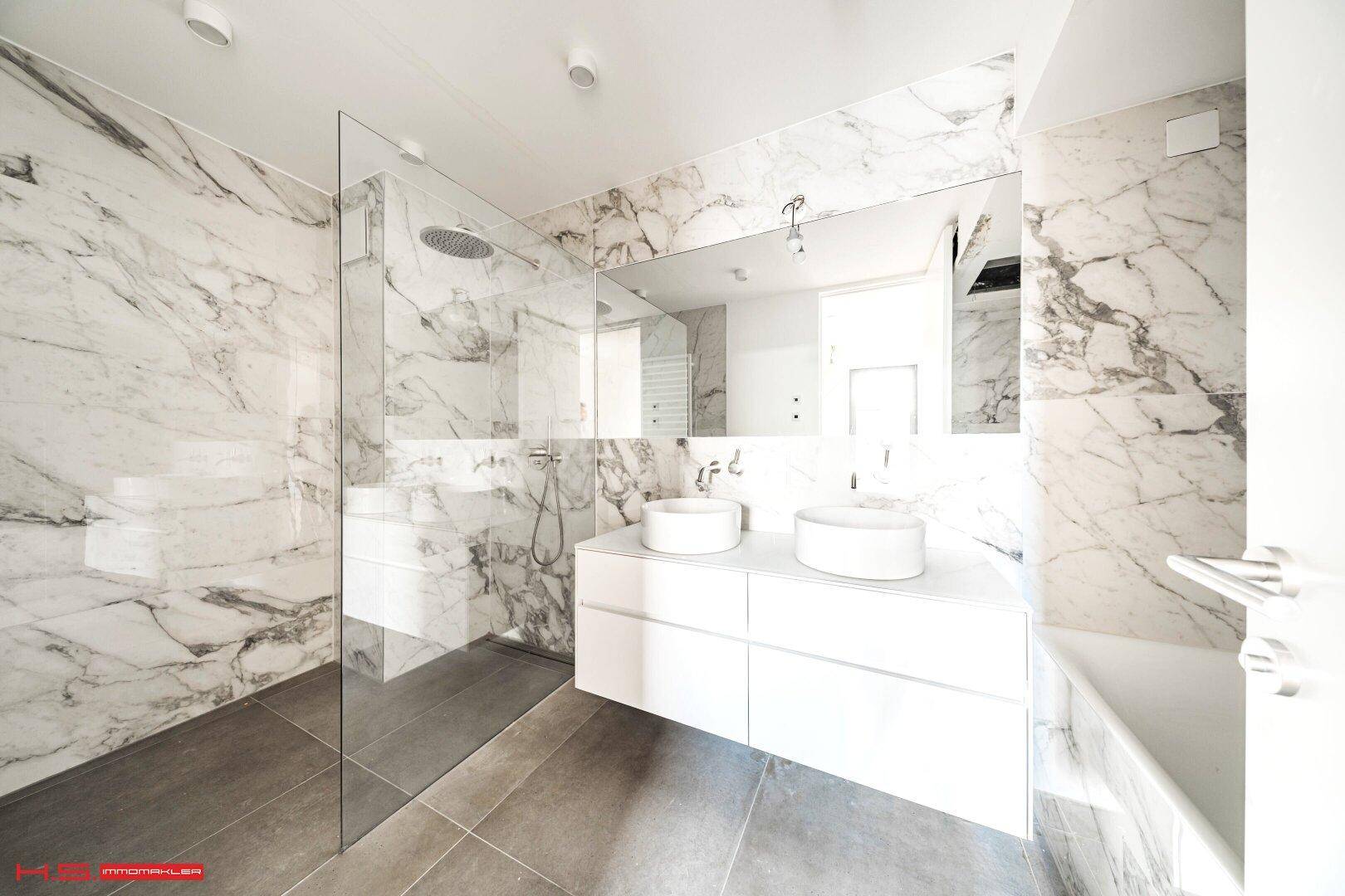 Modernes Badezimmer mit Marmoroptik-Fliesen, Doppelwaschbecken und begehbarer Dusche.