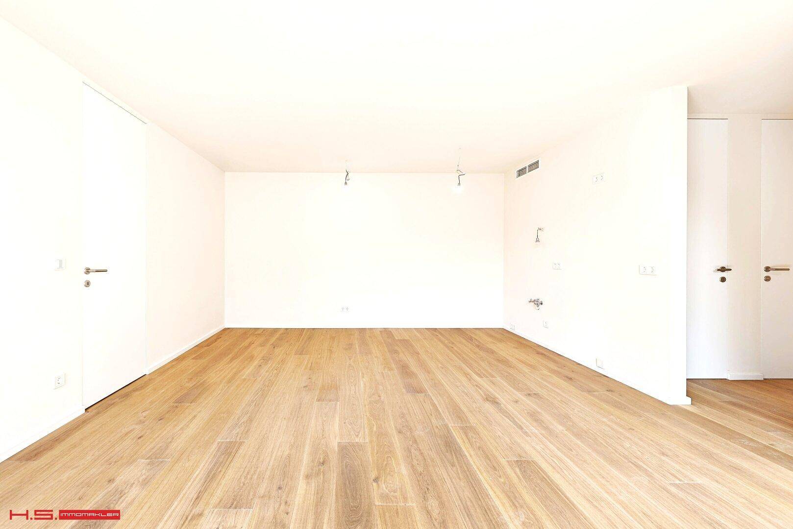 Leerer Küchenbereich mit Holzboden und Anschlüssen, bereit für die Installation einer Einbauküche.